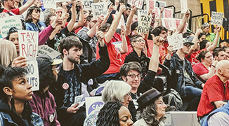 Image of a crowd holding "Tax the Rich" signs.
